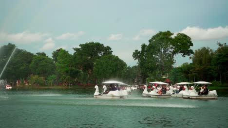 People-sailing-swan-boats-under-fountain-in-the-middle-of-the-lake-in-the-Lumpini-park,-Bangkok