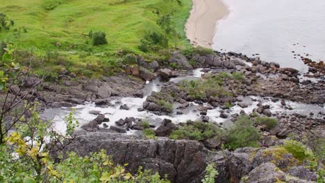 Felsiger-Fluss-Oder-Bach,-Der-An-Einem-Strand-In-Norwegen-Vom-Grasland-Ins-Meer-Fließt