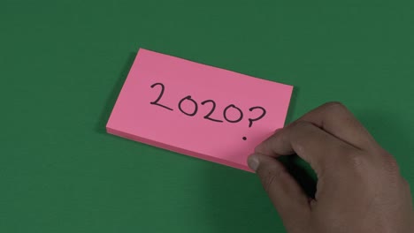Männliche-Linke-Hand-Schreibt-2020-Mit-Fragezeichen-Auf-Rosa-Post-it-Zettel