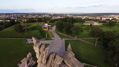 Memorial-of-the-Victims-of-Nazism-at-the-Ninth-Fort-of-Kaunas-city,-Lithuania-in-ascending-drone-aerial-shot-revealing-Kaunas-suburbs