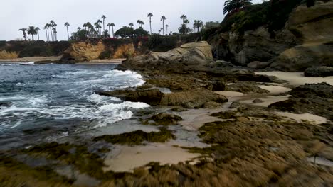 Low-flying-over-rocks-while-increasing-altitude-at-Laguna-Beach,-CA