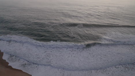 Schaumige-Wellen-An-Der-Küste-Mit-Alter-Dorflandschaft-Auf-Einem-Hügel-Am-Strand-Von-Nazare,-Portugal
