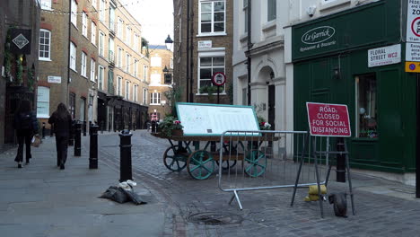 People-walk-past-a-road-sign-that-says,-“Road-closed-for-social-distancing”-in-a-very-quiet-Covent-Garden-during-the-second-national-Coronavirus-lockdown