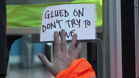 UK-November-2018---An-environmental-protestor-superglues-her-hand-with-a-note-that-says-“glued-on,-don’t-try-to-move”-to-a-window-of-the-UK-government-Department-for-Energy-offices