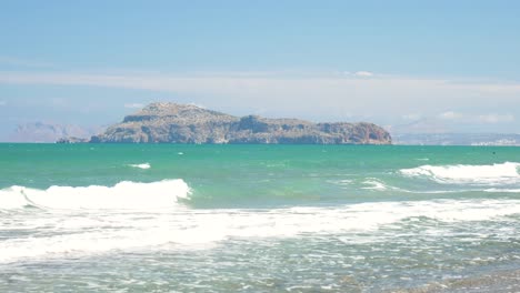 Island-called-Agioi-Theodoroi-in-the-background-as-waves-are-crashing-to-beach-while-turqouise-water-looking-warm-and-tempting-in-Crete-Greece