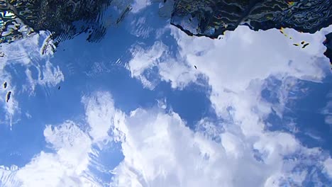 Cámara-Tendida-En-El-Fondo-De-Una-Piscina-Filmando-El-Cielo-Azul-Con-Nubes-Debajo-De-La-Superficie