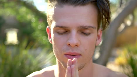 A-fit-young-attractive-white-man-smiling-and-closing-his-eyes-in-meditation-and-making-prayer-hands-while-focusing-on-present-awareness,-mindfulness,-positivity-and-good-vibes