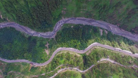 Aerial-view-of-a-curved-winding-roads-trough-the-forest-with-river,-Beautiful-nature-and-transportation-from-panoramic-view,-cars-are-going-through-the-road-on-the-mountain-with-green-forest