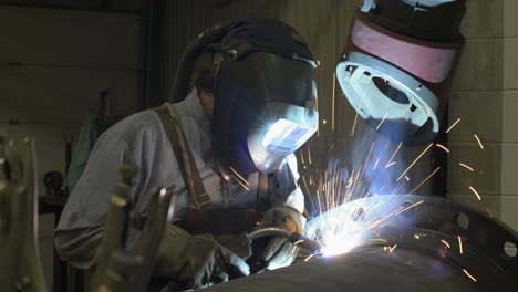 Sparks-fly-as-a-man-welds-a-large-pipe-in-an-industrial-machine-shop