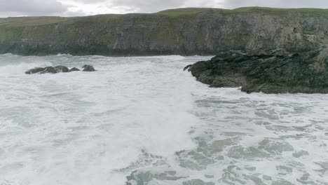 Aerial-tracking-in-sideways-on-with-waves-on-a-Scottish-rocky-beach-in-Sutherland