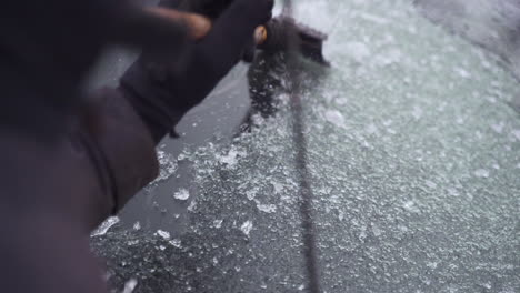 Man-cleaning-and-scraping-ice-from-car-windshield-in-snow