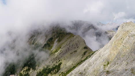 Time-lapse-of-clouds-moving-up-and-over-a-steep-ridgeline-with-large-mountains-in-the-background