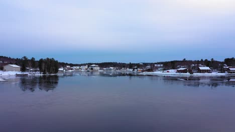 Aerial-footage-flying-low-over-a-skim-of-ice-on-Moosehead-Lake-towards-downtown-Greenville-Maine