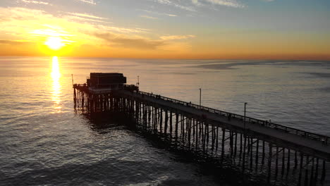 Drohnenaufnahmen-über-Dem-Newport-Beach-Pier-Mit-Menschen-In-Silhouetten-Während-Eines-Malerischen-Sonnenuntergangs-In-Südkalifornien-über-Dem-Ozean-Aus-Der-Luft