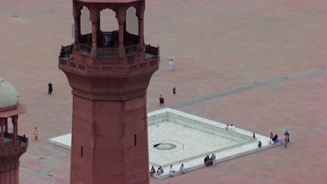 Lahore,-Pakistán,-Primer-Plano-Alejando-La-Vista-Aérea-De-Los-Minaretes-De-La-Mundialmente-Famosa-Mezquita-Badshahi,-Visitantes-Damas,-Caballeros-Y-Niños-Están-En-La-Mezquita,-Adoradores-En-El-Suelo-De-La-Mezquita