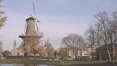Typische-Holländische-Windmühle-Mit-Dochten,-Die-Sich-In-Einem-Wohngebiet-In-Der-Stadt-Leiden,-Niederlande,-Im-Herbst-Mit-Fast-Blattlosen-Bäumen-Drehen