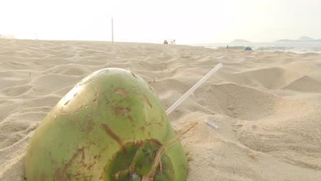 Eine-Einsame-Leere-Kokosnuss-Mit-Einem-Durchsichtigen-Plastikstrohhalm,-Der-Am-Strand-Zurückgelassen-Wurde