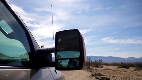 Looking-out-over-the-picturesque-California-desert-landscape-and-blue-sky-next-to-a-pickup-truck-rear-view-mirror-on-a-travel-camping-trip