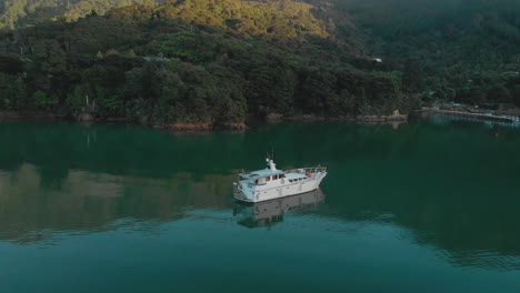 Morning-aerial-flying-around-cruise-boat-anchored-in-bay-in-Marlborough-Sounds,-New-Zealand