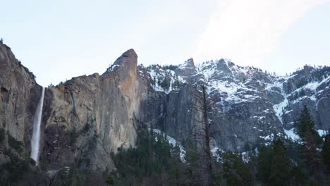 Schwenkaufnahme-Der-Schneebedeckten-Gipfel-Im-Yosemite-Nationalpark,-Die-Die-Bridalveil-Fälle-Nach-Sonnenuntergang-Sichtbar-Macht