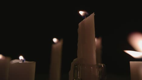 An-extreme-close-up-and-pan-across-of-white-candles-lit-with-a-black-background-in-slow-motion