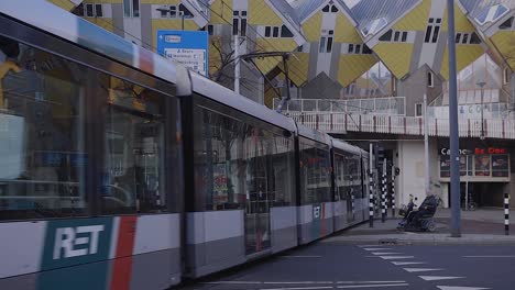 Tram-passing-by-continuing-underneath-the-overhead-famous-architecture-of-the-overhanging-cube-houses-in-the-city-centre-of-Rotterdam,-The-Netherlands
