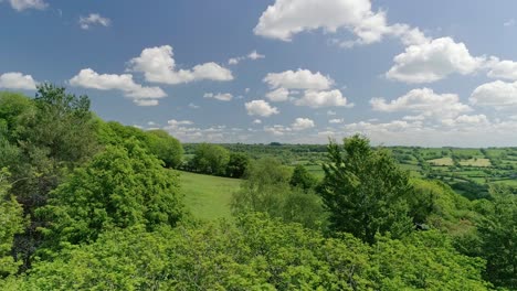 Langsamer-Weg-Vorbei-An-Baumwipfeln-Zwischen-Grünen-Englischen-Feldern-Und-Einer-Weiten-Landschaft-Mit-Einem-Malerischen-Blauen-Himmel-Mit-Bauschigen-Wolken