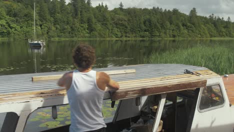 Wide-shot-young-man-removing-masking-tape-from-cabin-roof-of-wooden-boat