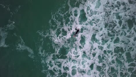Birds-eye-view-of-surfer-duck-diving-choppy-waves.-Drone-shot