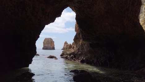 Viewing-out-the-mouth-of-an-Algarve-sea-cave-to-a-limestone-rock-stack,-Portugal