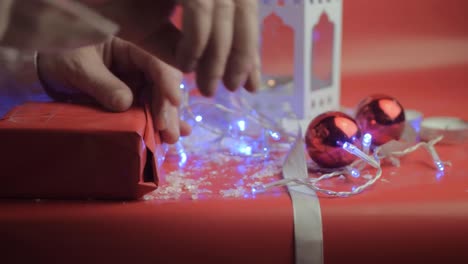 Wrapping-Christmas-gift-with-ribbons-and-red-paper-with-red-background-and-baubles