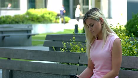 Young-woman-sitting-on-bench-and-texting-on-her-cellphone