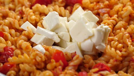 Putting-chunks-of-mozarella-cheese-in-pan-with-cooked-fusilli-pasta-with-tomato-sauce,-close-up-shot-in-slow-motion