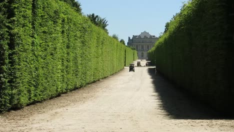 Gerader-Weg-Aus-Sand-Mit-Golfautos,-Die-Sich-Bewegen,-Mit-Dem-Schloss-Von-Versailles-Im-Hintergrund