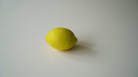 Male-hand-spinning-a-whole-lemon-in-slow-motion-on-a-white-table-with-shadows-then-takes-the-lemon-off-the-table-perfect-shot-of-copy-text