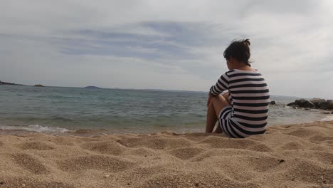 Szenische-Nette-Junge-Frau,-Die-Am-Strand-In-Sithonia,-Griechenland,-Statische-Rückseite-Sitzt