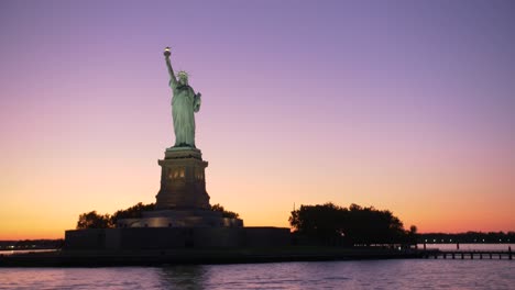 establishing-shot-of-Statue-of-liberty-silouhette-at-dawn,-shot-from-a-boat-on-orange-and-violet-sky