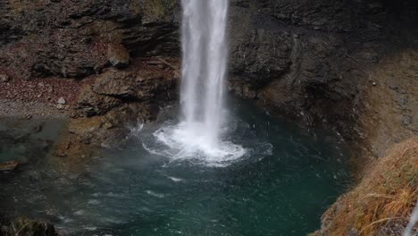 Zeitlupenaufnahme-Eines-Wasserfalls-Auf-Einer-Felsigen-Rötlichen-Klippe-Und-Klarem-Wasser
