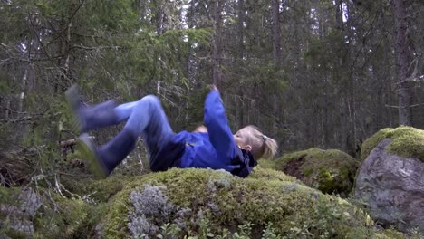 Young-boy-with-ponytail-doing-parkour-in-mossy-forest