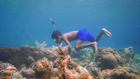 Un-Niño-Pequeño-Está-Pescando-Con-Su-Fusil-Casero-Entre-Arena-Negra-Y-Corales