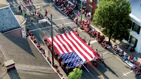 Aerial-of-4th-of-July-parade,-Boy-Scouts-carry-large-American-flag,-Cub-Scouts-follow-behind,-star-spangled-banner