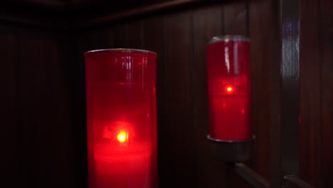 Two-red-candles-that-burn-in-a-church-behind-a-wood-wall
