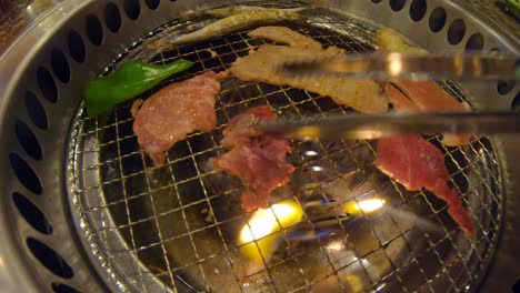 Tongs-flipping-grilled-meat-on-sizzling-hot-yakiniku-Japanese-BBQ