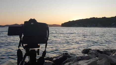 Camera-standing-on-dark-tripod-shooting-timelaps-at-sunset