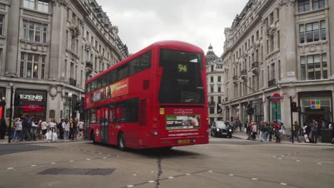 Red-double-decker-turning-Oxford-Street-in-London,-lot-of-cars-and-people-around