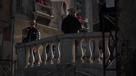 Venice-Italian-Gondoliers-interacting-with-passing-tourists-on-ornate-canal-bridge-waterway-passage