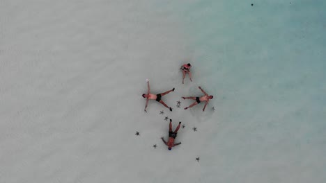 4K-aerial-of-four-people-floating-on-their-backs-near-the-beach-surrounded-by-star-fish