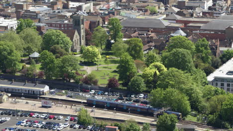 Tracking-aerial-view-of-a-commuter-train-leaving-Maidstone-East-station-and-crossing-the-River-Medway-in-Maidstone,-Kent