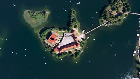 AERIAL:-Very-High-Altitude-Top-View-of-Trakai-Island-Castle-with-Boats-Sailing-Around-it-and-Visible-Isolated-Islands-with-Growing-Trees