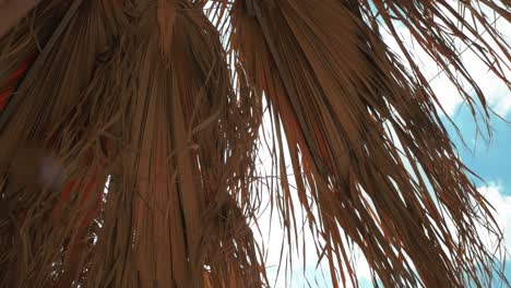 Palmenschirm-Am-Griechischen-Strand-Mit-Blauem-Himmel-Und-Weißen-Wolken,-Während-Eine-Leichte-Brise-Weht